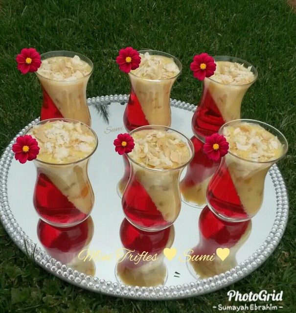 four glasses filled with dessert sitting on top of a white plate in the middle of grass