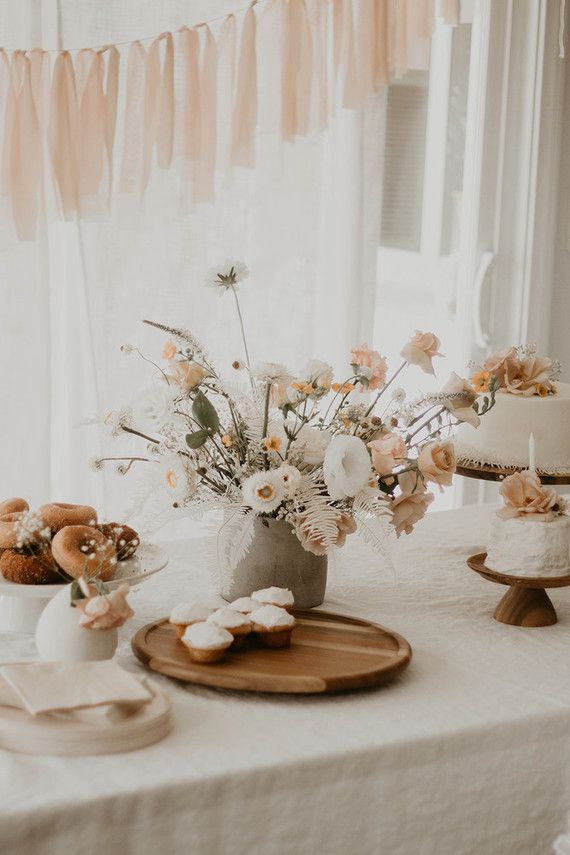 a table topped with a cake and flowers on top of a white table cloth covered table