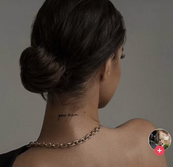 the back of a woman's neck with a cross tattoo on her left shoulder