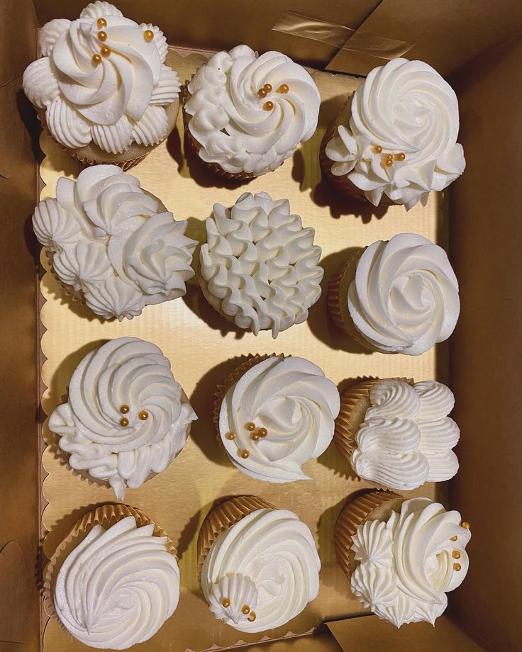 a box filled with white frosted cupcakes on top of a table