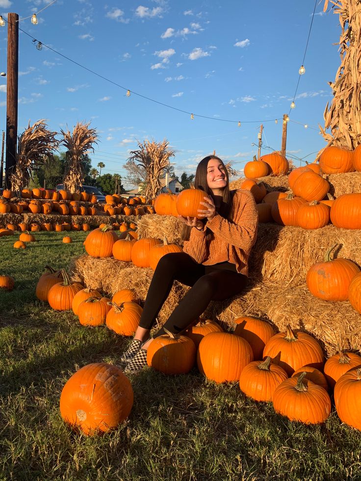 a woman sitting on hay bales surrounded by pumpkins