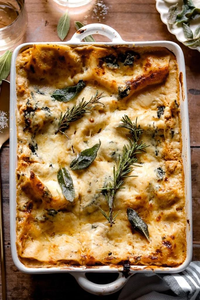 a casserole dish with cheese and herbs in it on a wooden table next to utensils