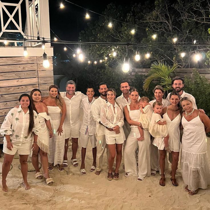 a group of people dressed in white posing for a photo on the beach at night