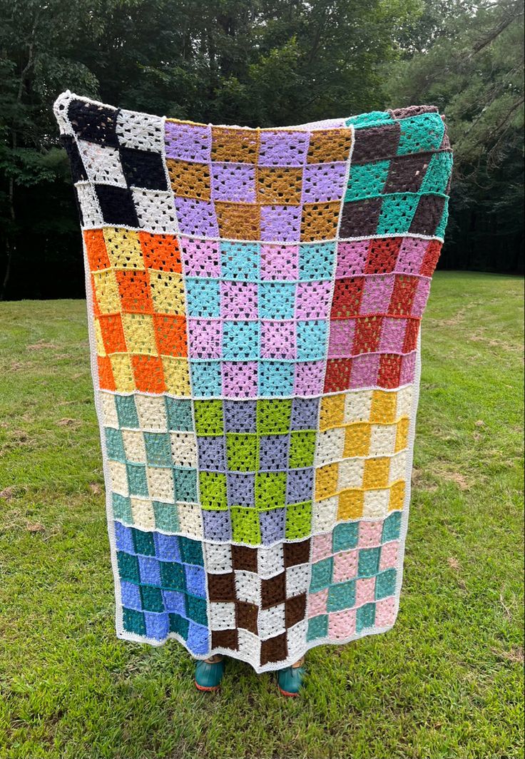 a crocheted blanket sitting on top of a grass covered field