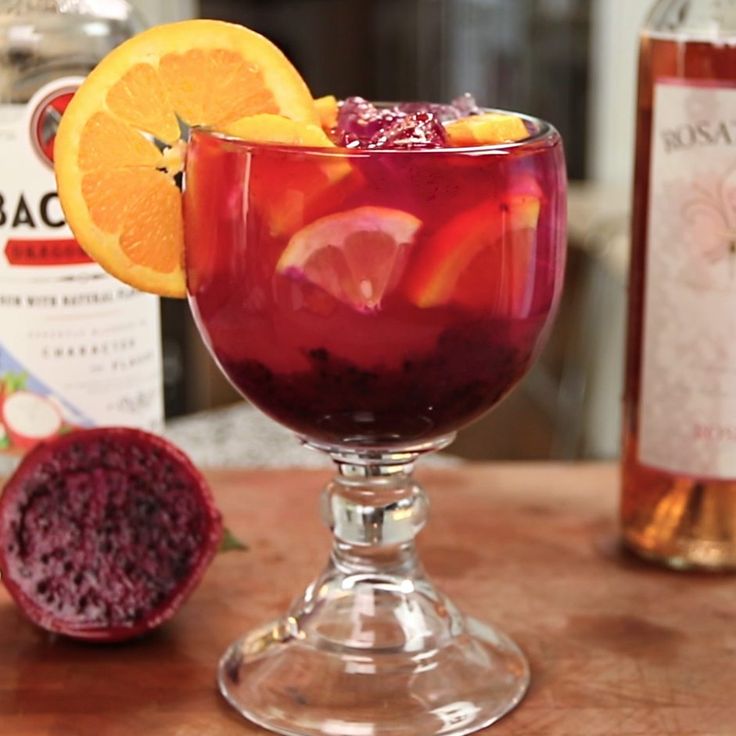 a glass filled with red liquid and garnished with orange slices next to a bottle of booze