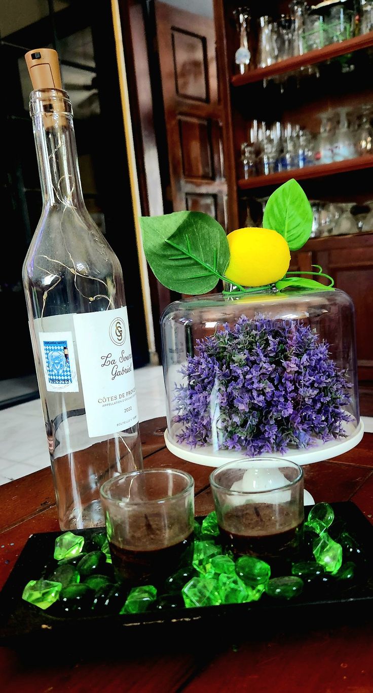 there is a bottle and two glasses on the table next to each other with flowers in them