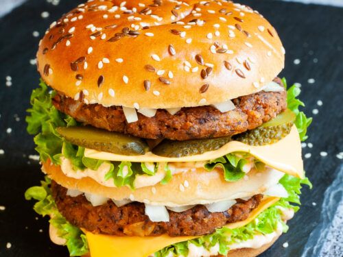 a hamburger with cheese and pickles on it sitting on top of a black surface