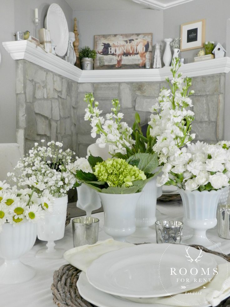 the table is set with white dishes and flowers