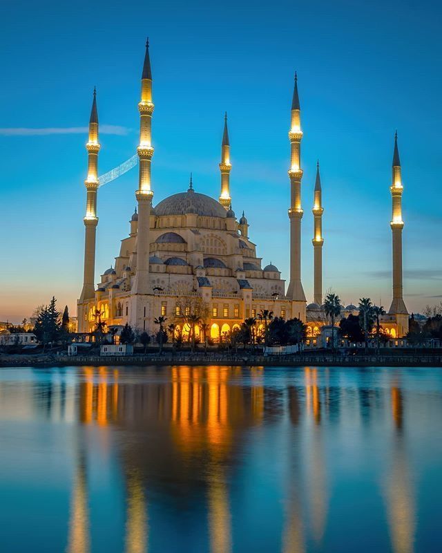 the blue mosque is lit up at night with its lights on and reflecting in the water