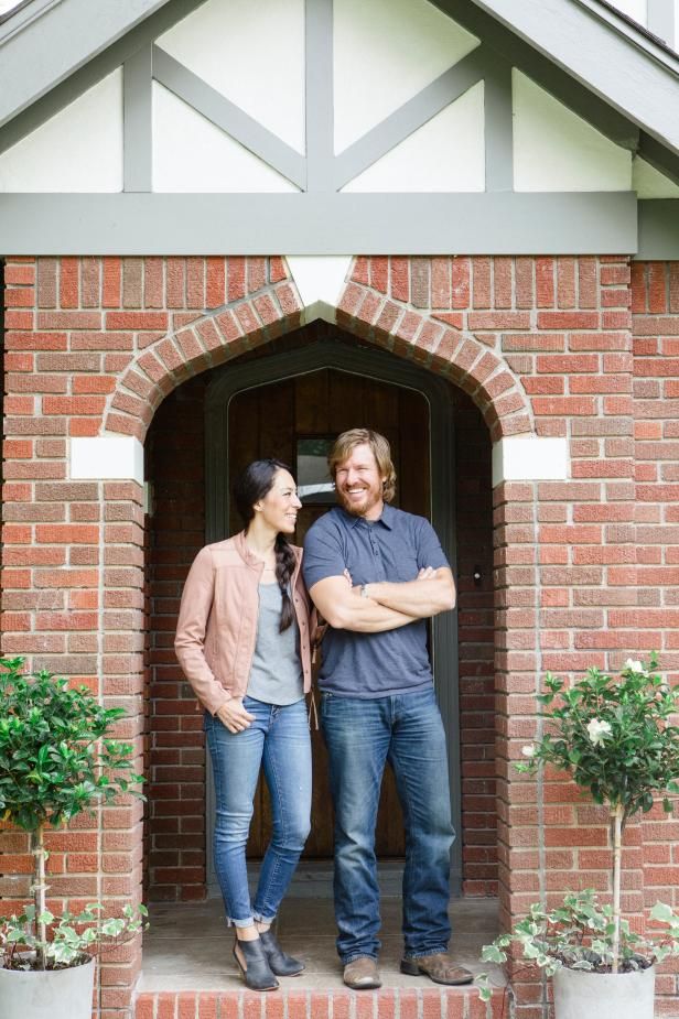 a man and woman standing in front of a brick building with potted plants on either side