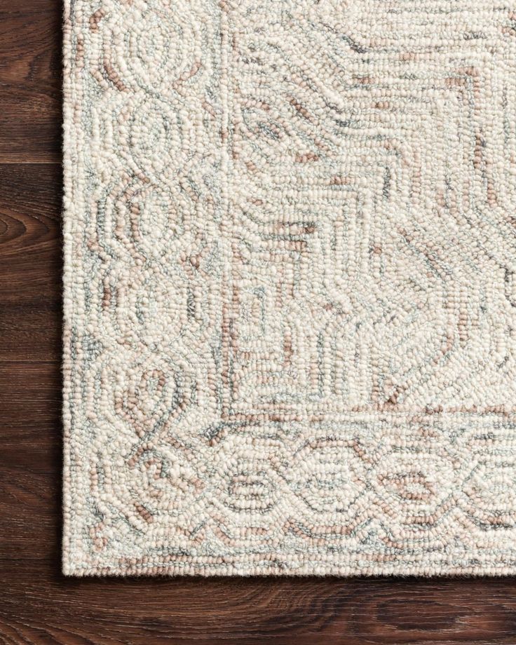 a white rug with an intricate design on top of a wooden floor next to a plant