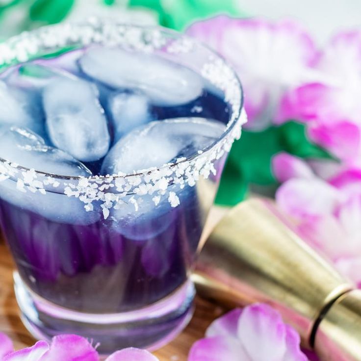 a purple drink with ice and sprinkles in a glass on a wooden board