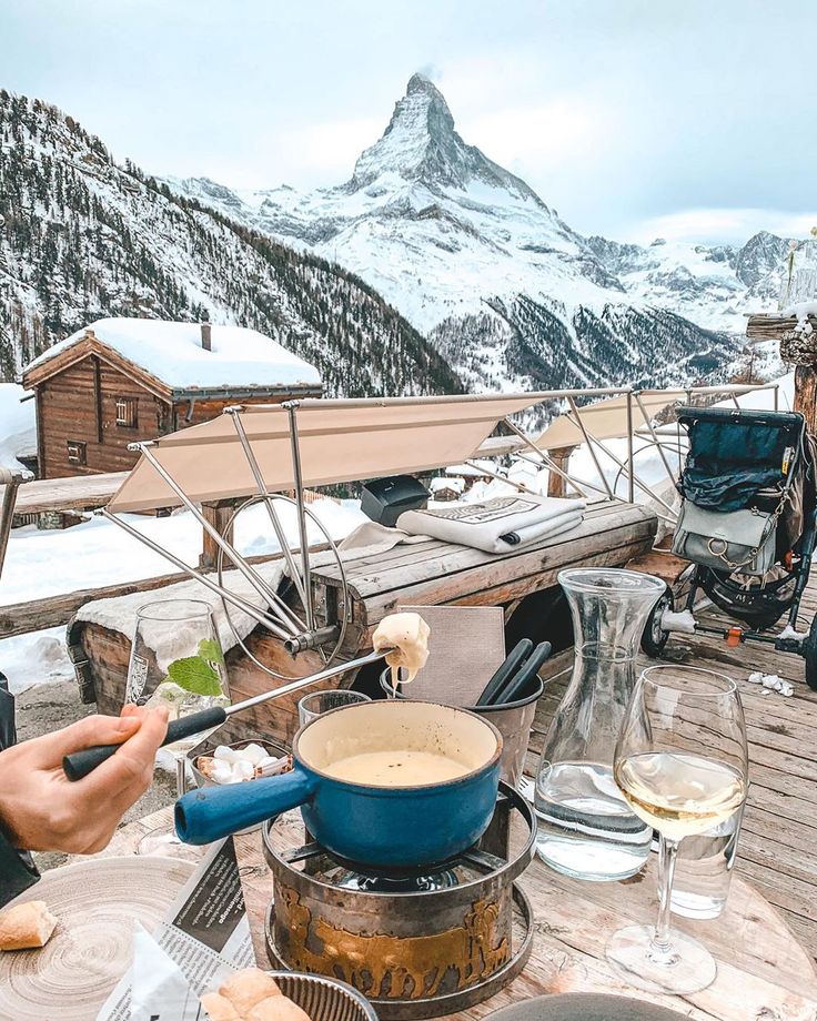 a table with food and drinks on it in front of a mountain range covered in snow