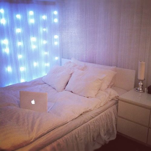 a laptop computer sitting on top of a bed next to a window with light curtains