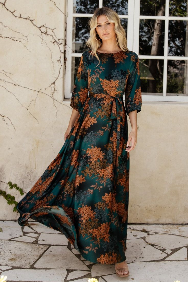 a woman standing in front of a window wearing a green and orange floral print dress