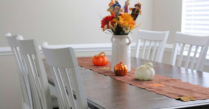 a dining room table with white chairs and fall decorations