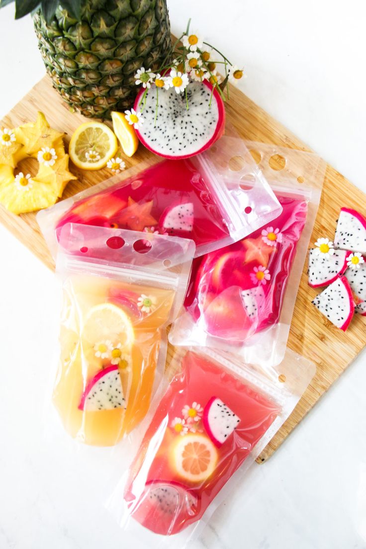 various fruits are packaged in plastic bags on a cutting board next to a pineapple