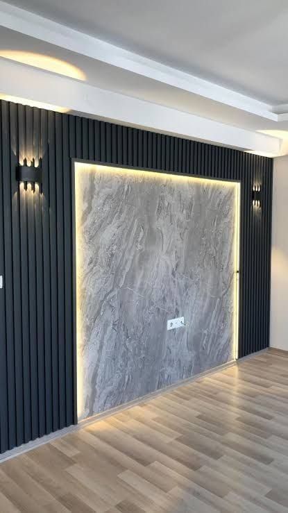 an empty room with wood flooring and black paneling on the walls, along with two wall sconces