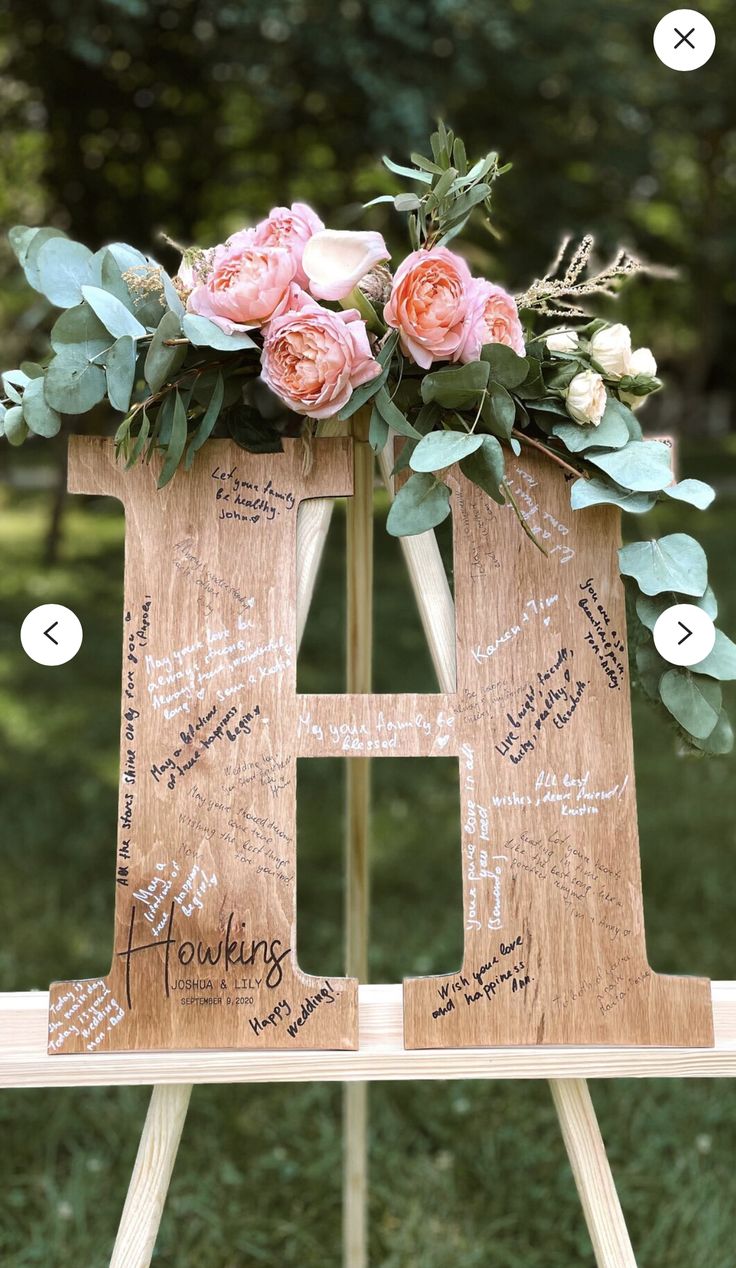 a wooden easel with flowers and greenery on it, labeled in the letter h