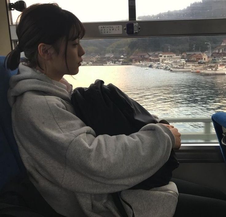 a woman is sitting on a bus looking out the window at boats in the water