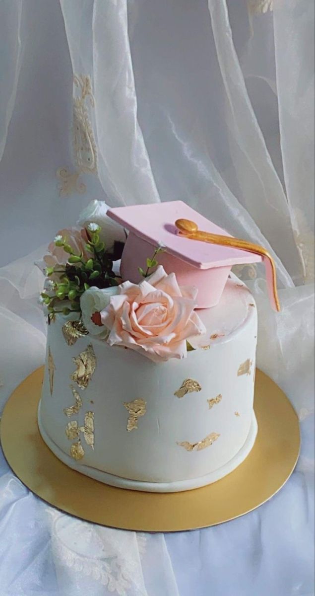 there is a cake with flowers and a graduation cap on the top, sitting on a gold plate