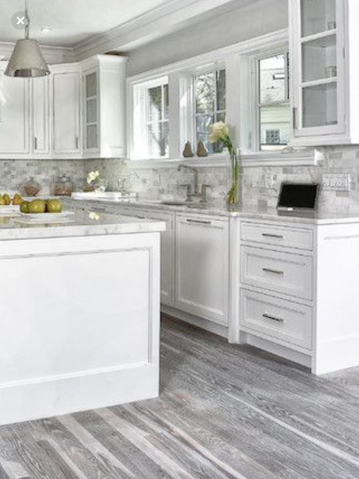 a kitchen with white cabinets and marble counter tops, an island in the middle is surrounded by wood flooring