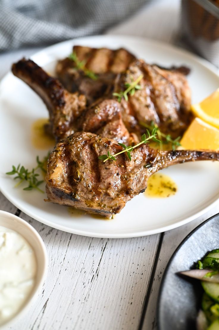 two pieces of lamb chops on a white plate with lemon wedges next to it