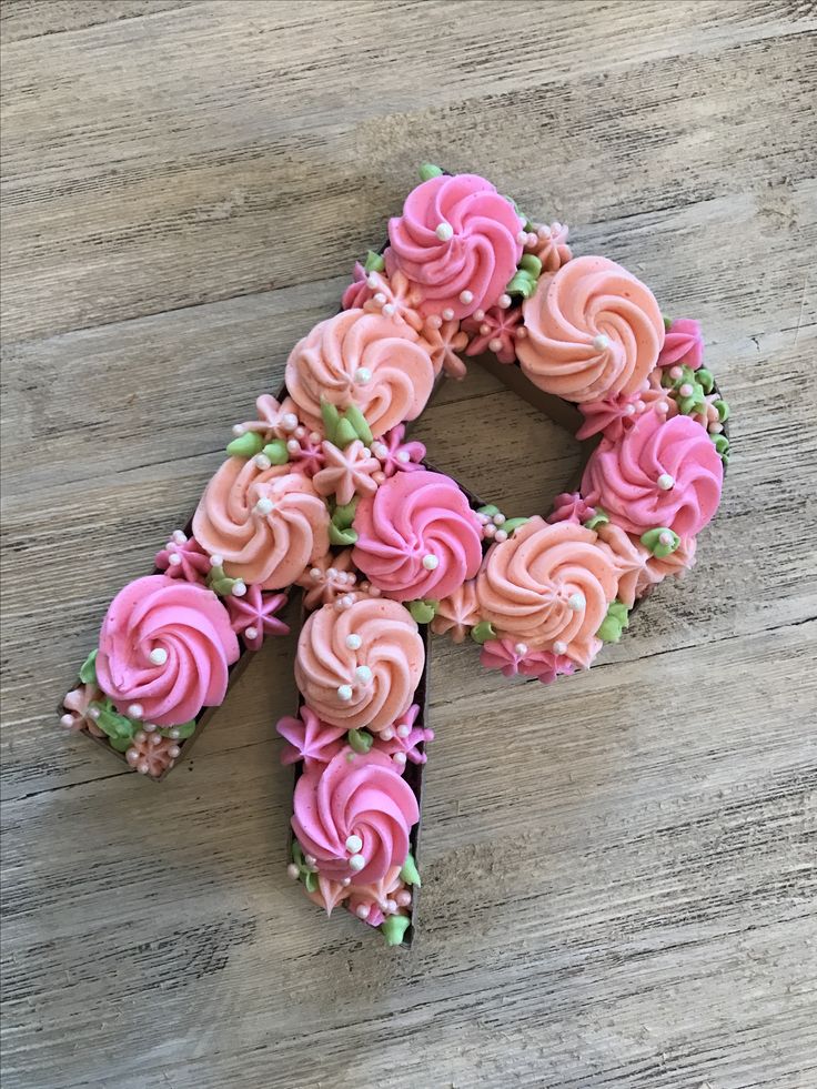 pink frosted cupcakes arranged in the shape of an x on a wooden surface