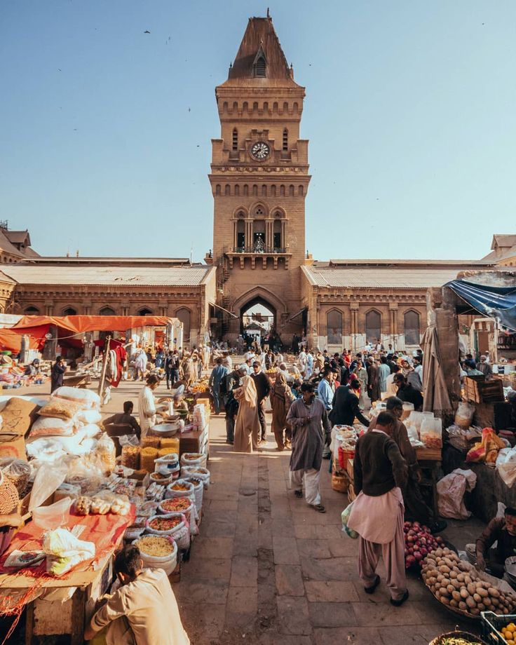 an outdoor market with people walking around and vendors selling goods in front of the clock tower