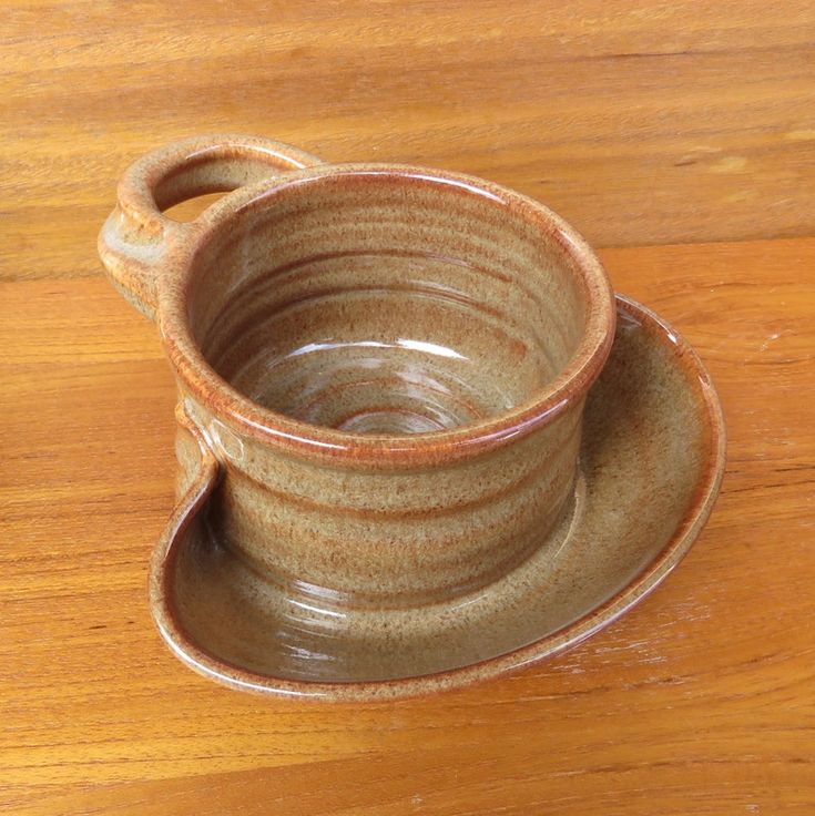 a brown cup and saucer sitting on top of a wooden table next to each other