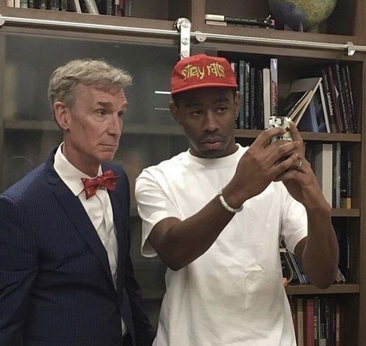 two men standing next to each other in front of a book shelf