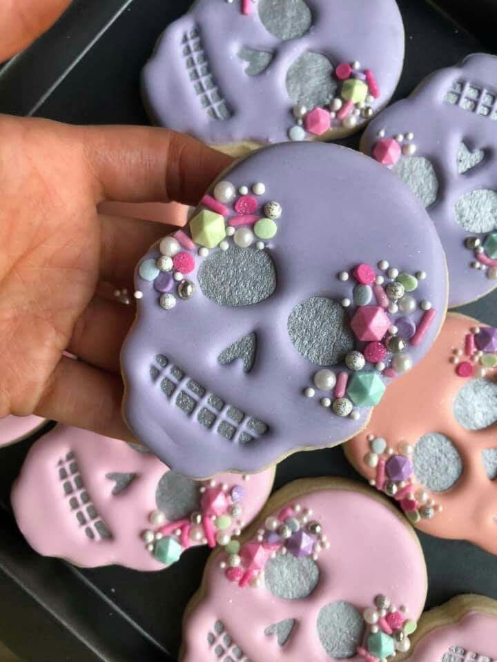 decorated sugar cookies in the shape of skulls are being held by someone's hand