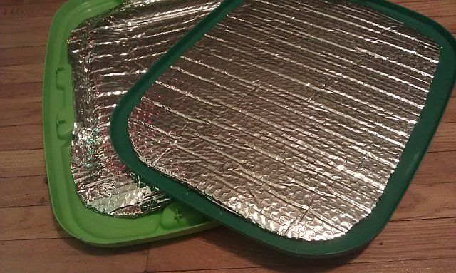 two green trays filled with aluminum foil on top of a wooden floor next to each other