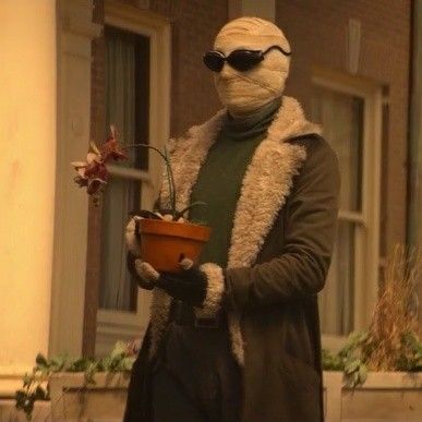 a man wearing a mask and holding a potted plant in front of a building