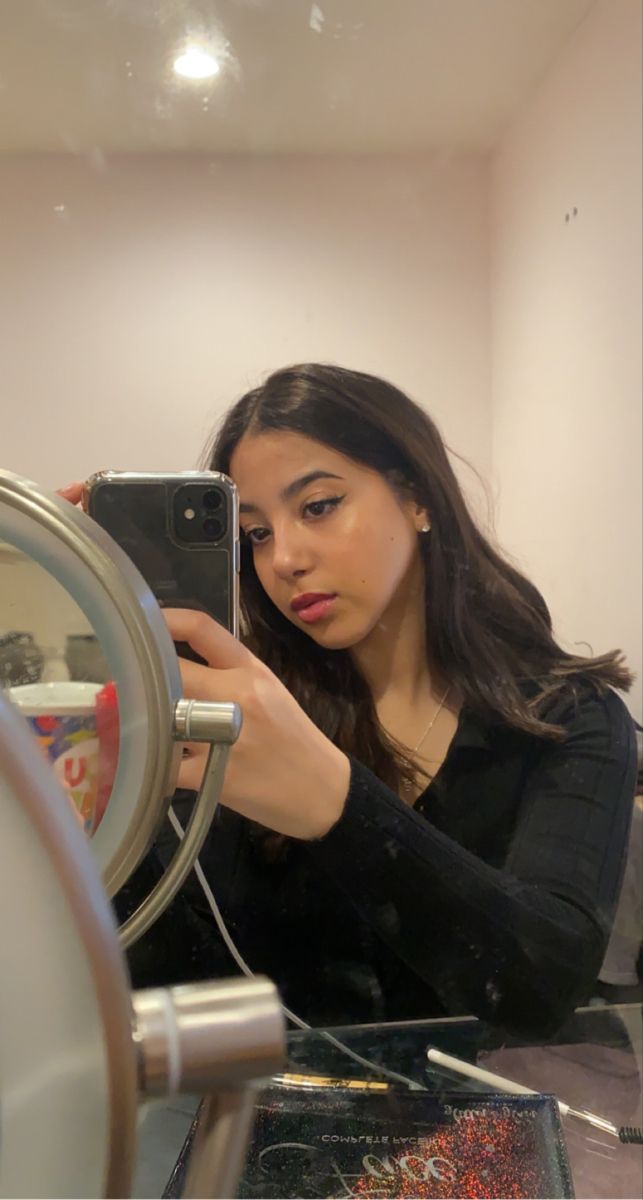 a woman taking a selfie with her cell phone in front of a mirror that is hanging on the wall