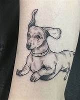 a small dog tattoo on the wrist is shown in black and grey ink, with a collar around it's neck