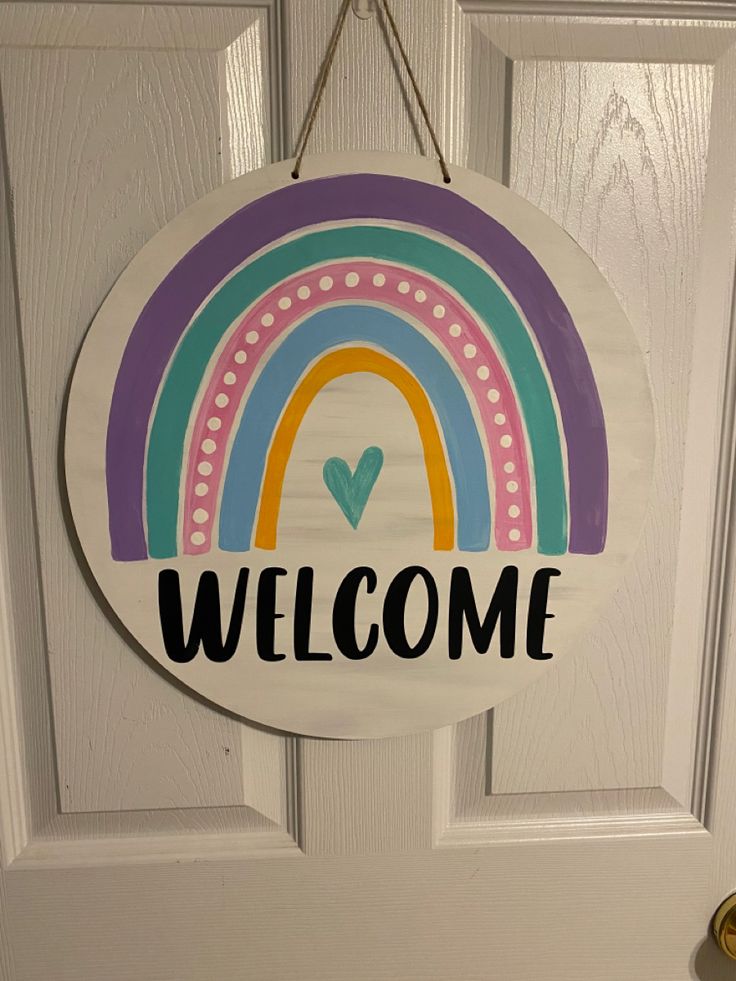 a welcome sign hanging on the front door to someone's house with a rainbow painted on it