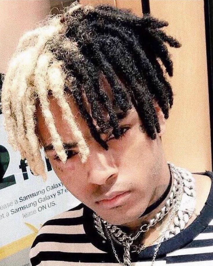 a young man with dreadlocks looks at his cell phone while wearing a black and white striped shirt