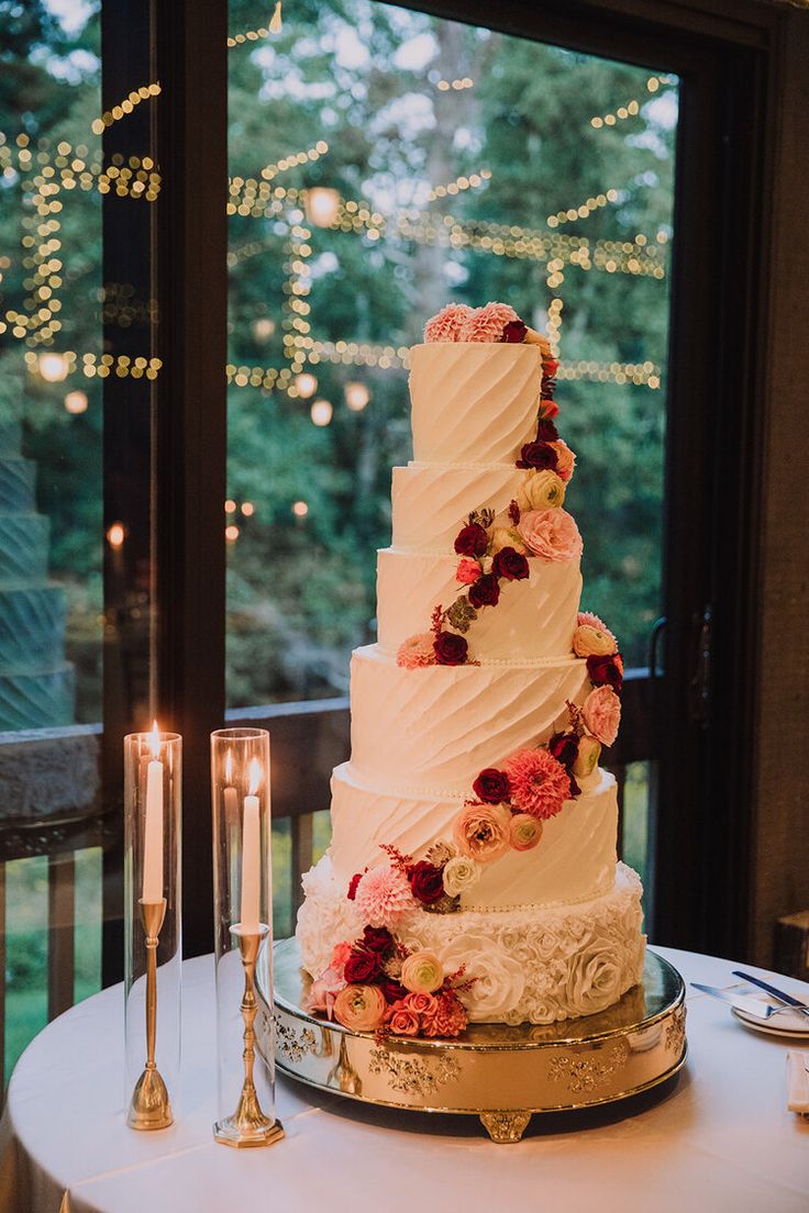 a wedding cake sitting on top of a table next to two candles and a window