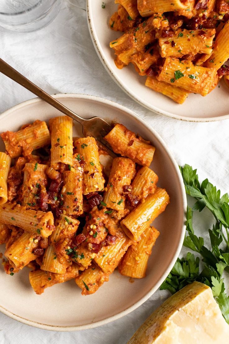 two plates of pasta with sauce and parmesan cheese on the side next to a lemon wedge