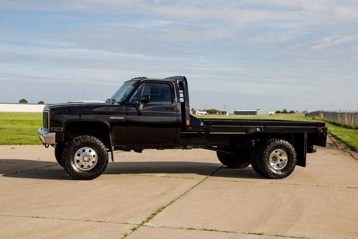 a black pickup truck parked on top of a cement lot next to a green field