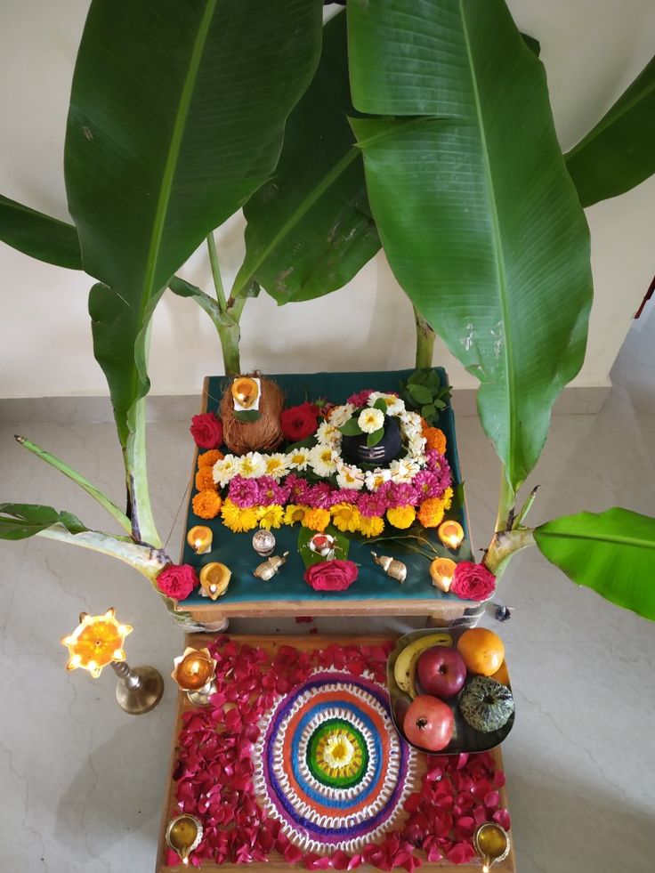 an arrangement of flowers, candles and fruit on a table next to a potted plant