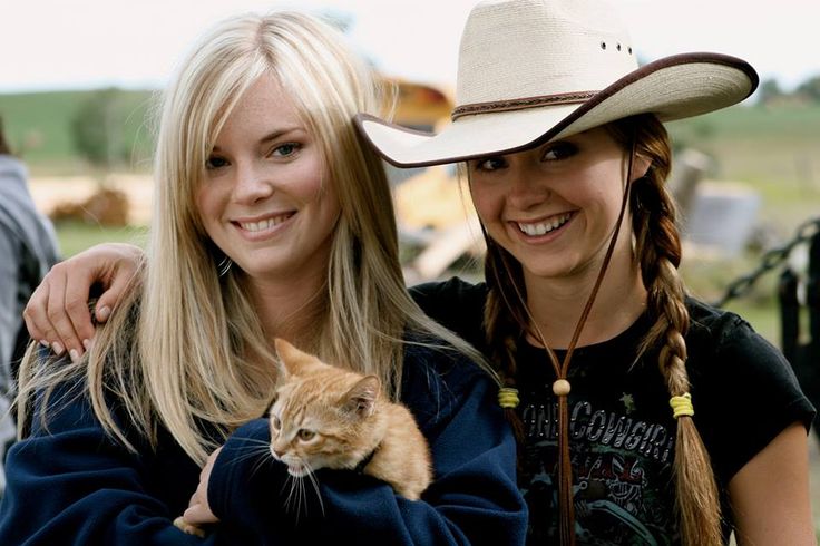 two beautiful women standing next to each other with a cat in their arms and smiling