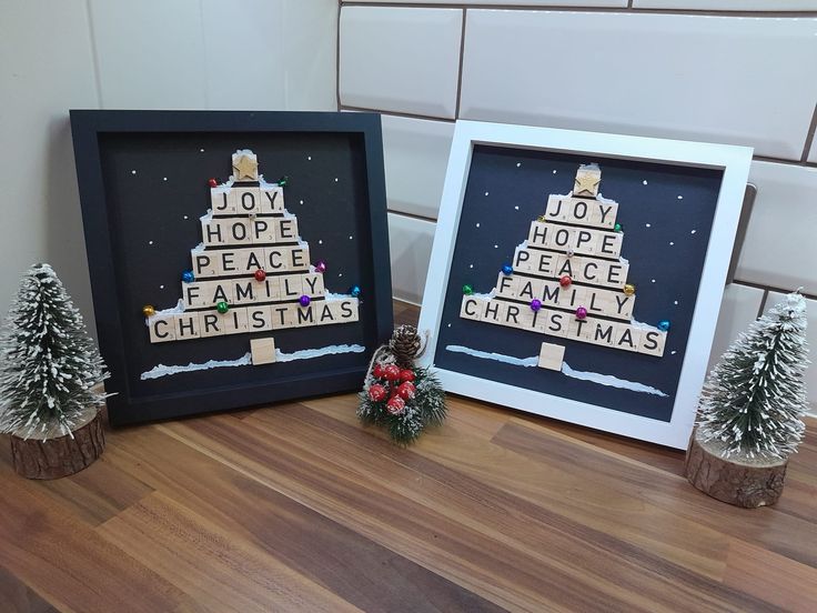 two framed cross stitch christmas trees on a wood floor next to each other, with the words joy hope peace family christmas