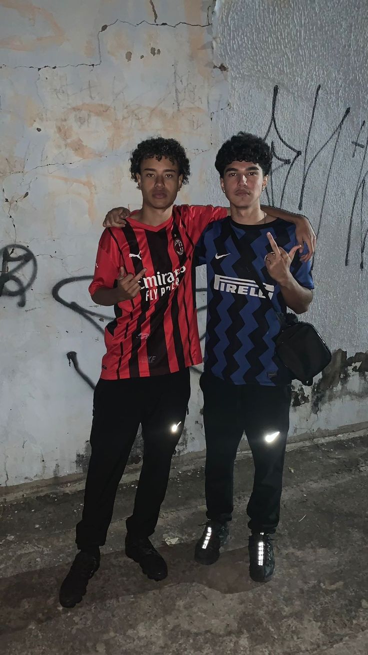 two young men standing next to each other in front of a wall with graffiti on it