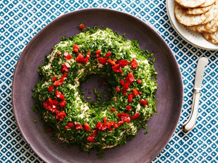 a purple plate topped with a green wreath covered in red peppers next to a fork and knife