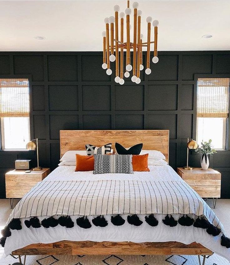 a bedroom with black walls, white bedding and a wooden headboard that has pom poms on it