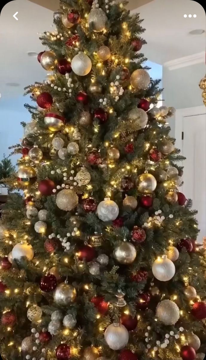 a christmas tree is decorated with red and gold ornaments, while the lights are on