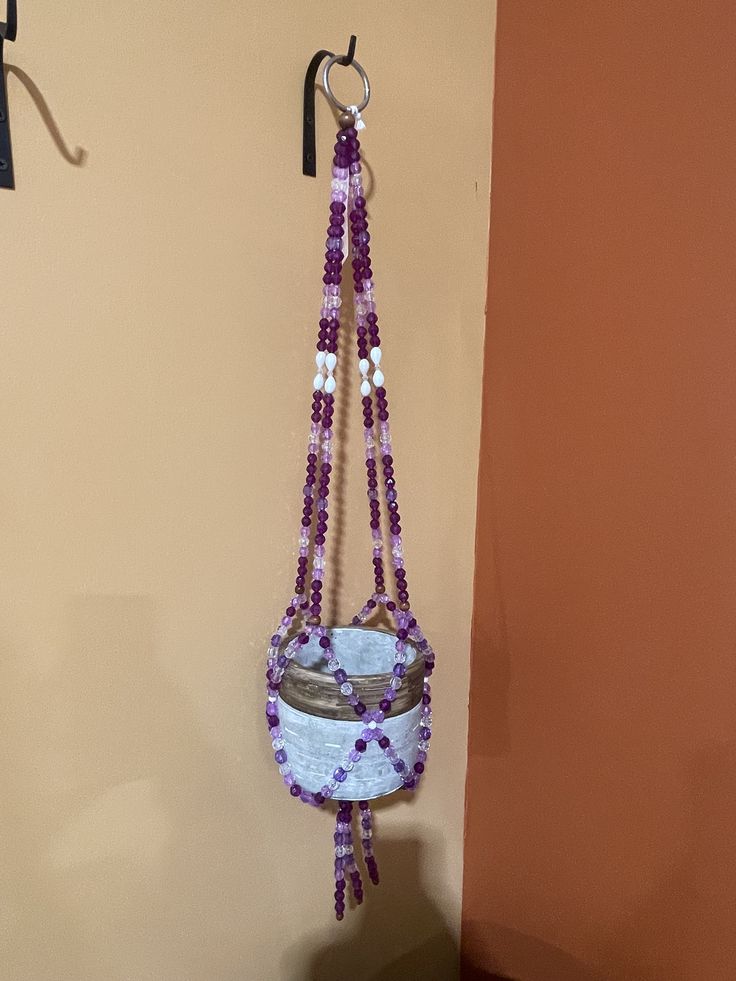 a purple and white beaded hanging from a hook on the side of a wall