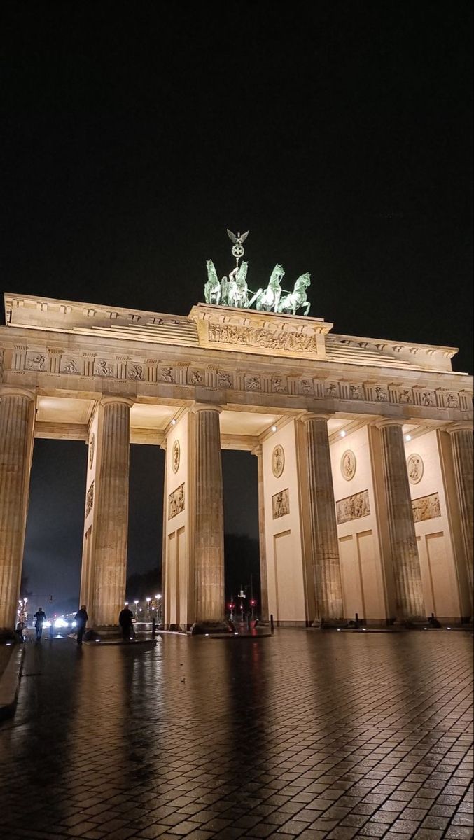 the building is lit up at night and has statues on it's front entrance